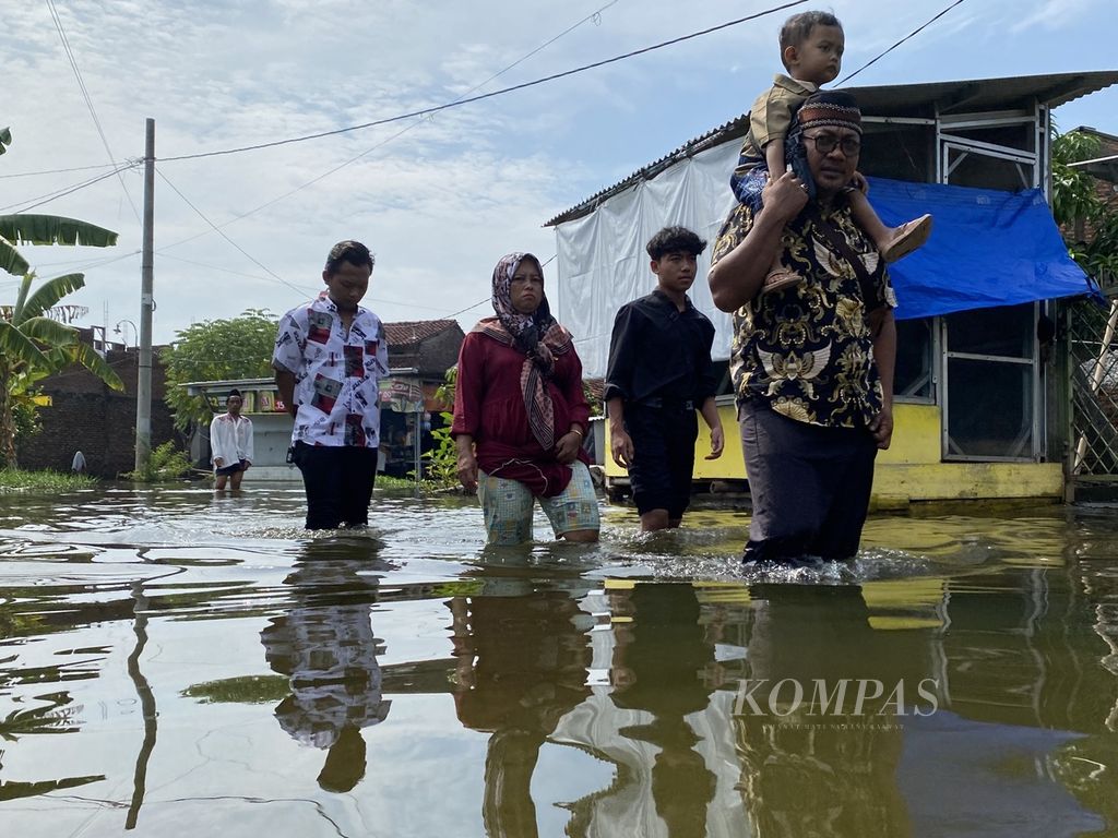 Rombongan warga menerjang banjir di Desa Sayung, Kecamatan Sayung, Kabupaten Demak, Jawa Tengah, Rabu (10/4/2024), untuk bersilaturahmi dan bermaaf-maafan di rumah kerabatnya. Warga berharap, pemerintah menambah jumlah pompa air yang beroperasi di wilayah itu untuk mengurangi genangan. 