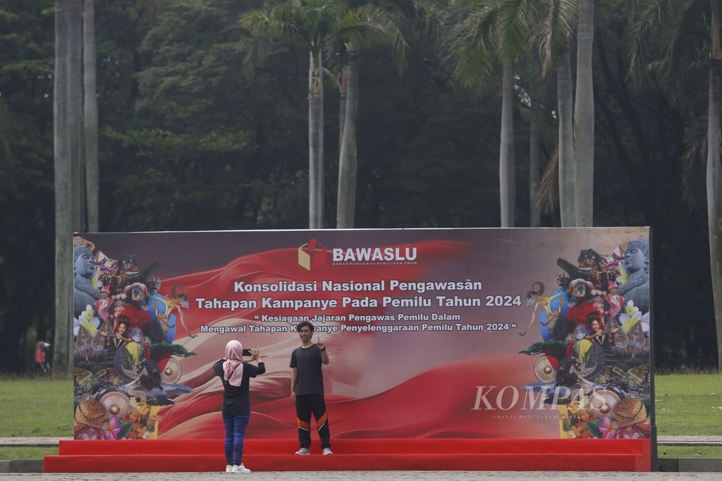 Warga berfoto di depan baliho Apel Siaga Pengawasan Tahapan Kampanye Pemilu 2024 di Monumen Nasional (Monas), Jakarta, Minggu (26/11/2023). Apel ini dihadiri oleh jajaran Bawaslu dari semua provinsi di Indonesia.