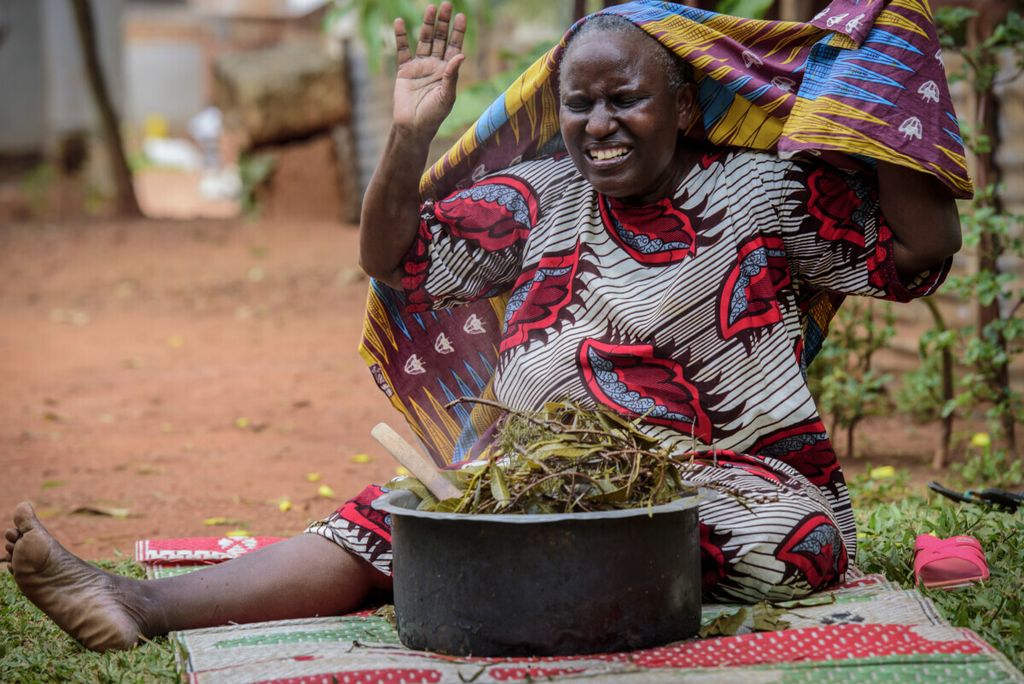 Seorang perempuan melambaikan tangan sambil tersenyum setelah menghirup uap dari ramuan herbal lokal yang diyakini bisa mencegah dan meringankan gejala Covid-19 di Kampala, Uganda, 6 Juli 2021. 