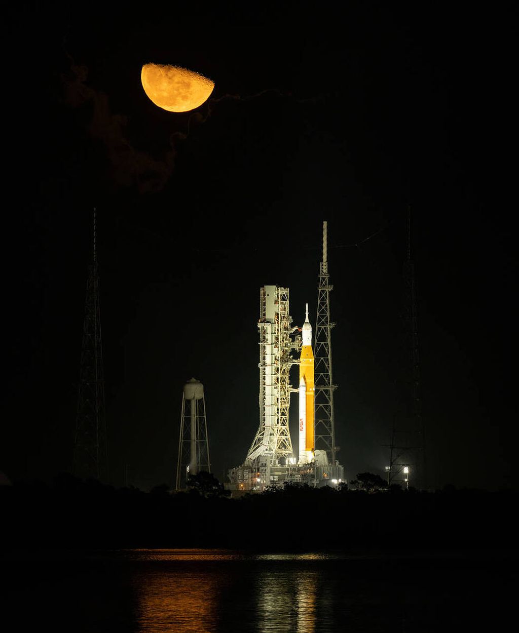 Bulan tampak di atas roket peluncur Sistem Peluncuran Luar Angkasa (Space Launch System) yang terparkir di landas luncur 39B Bandar Antariksa Kennedy, Florida, AS, pada Senin (14/11/2022) atau dua hari sebelum jadwal peluncurannya. Di bagian atas roket ada wahana antariksa Orion yang akan terbang menuju Bulan.