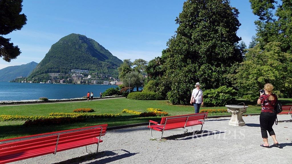Wisatawan berpose di salah satu sudut Parco Civico-Vila Ciani dengan latar Danau Lugano, Swiss, pada pertengahan Juni tahun 2018. 