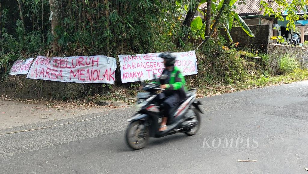 Seorang pengendara sepeda motor melintas di depan spanduk penolakan rencana pembukaan tempat penampungan sampah sementara di Dusun Karanggeneng, Desa Umbulharjo, Kecamatan Cangkringan, Kabupaten Sleman, Daerah Istimewa Yogyakarta, Rabu (26/7/2023). 