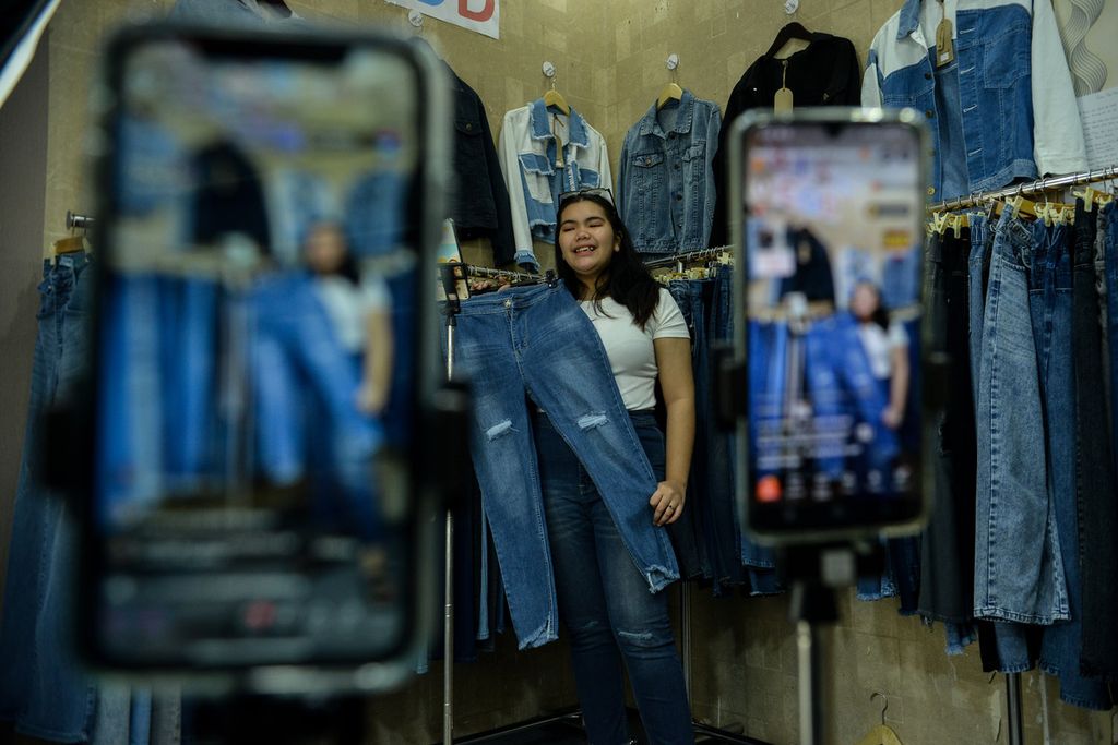 Pedagang menawarkan celana kepada pengguna media sosial Tiktok saat siaran langsung di kios Blok B Tanah Abang, Jakarta, Selasa (13/6/2023). Penjualan secara daring menjadi salah satu strategi para pedagang untuk menjangkau konsumen yang lebih luas. Salah seorang pedagang mengatakan, 40-50 persen pendapatannya berasal dari penjualan secara daring. 
