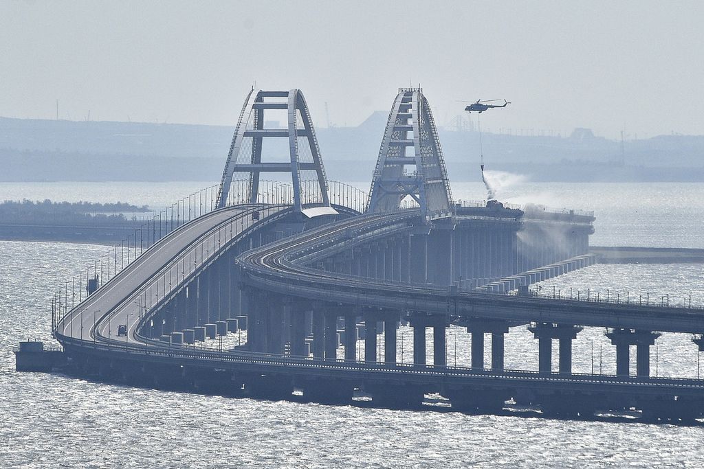 Sebuah helikopter menurunkan air untuk menghentikan kebakaran di Jembatan Crimea yang menghubungkan Rusia dan Semenanjung Crimea di atas Selat Kerch, 8 Oktober 2022. Pada 17 Juli 2023, terjadi ledakan lagi di jembatan tersebut. 