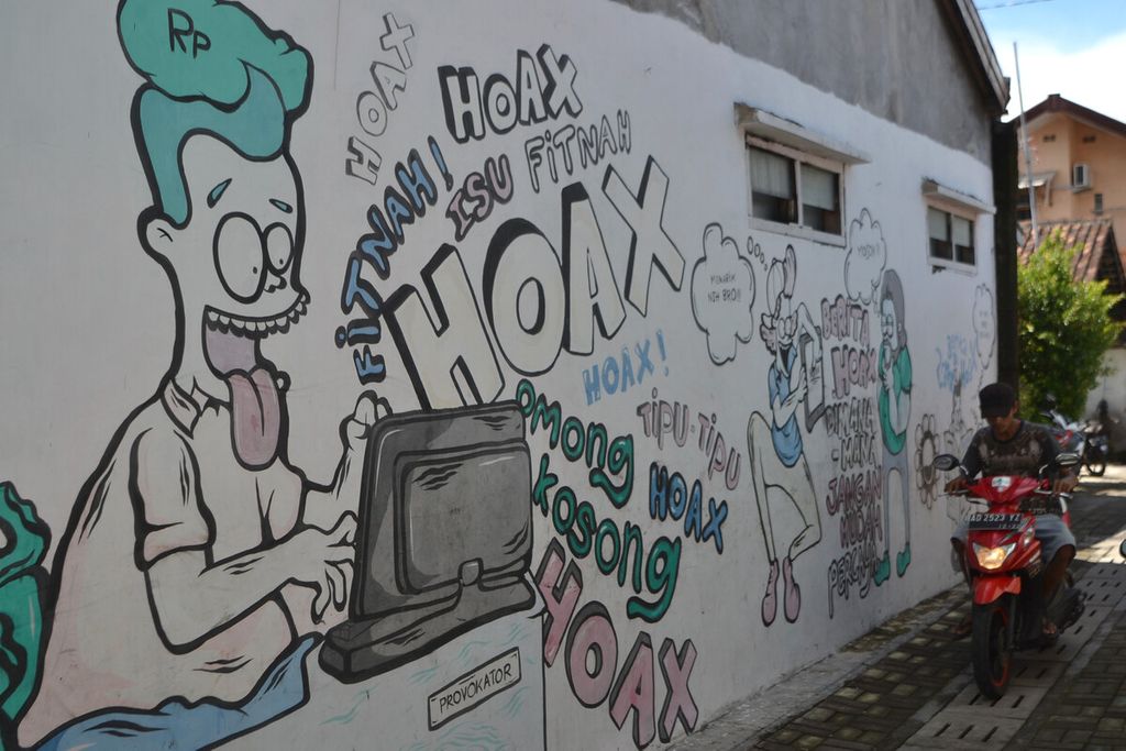 Warga melintas di dekat mural berisi ajakan menghindari berita hoaks di Kelurahan Gandekan, Jebres, Solo, Jawa Tengah, Senin (10/2/2020). 