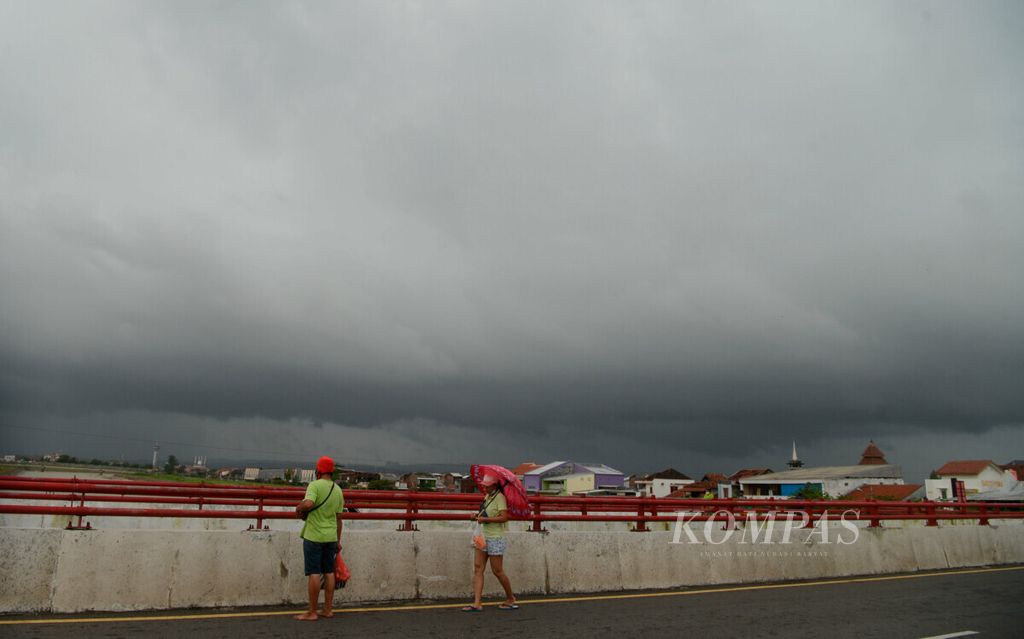 Warga berjalan di atas jembatan Banjir Kanal Timur dengan latar belakang cuaca mendung di Kota Semarang, Jawa Tengah, Minggu (7/2/2021). Dalam beberapa hari ini, cuaca ekstrem dengan curah hujan tinggi terjadi di sejumlah wilayah Jawa Tengah hingga berpotensi bencana.
