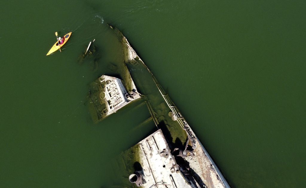 Seorang warga Serbia, Aleksandar Bzdusok dengan menggunakan kayak mendayung di sebelah bangkai sebuah kapal perang milik Nazi Jerman yang ditenggelamkan di Sungai Danube, tak jauh dari Prahovo, Serbia pada Jumat (26/8/2022).
