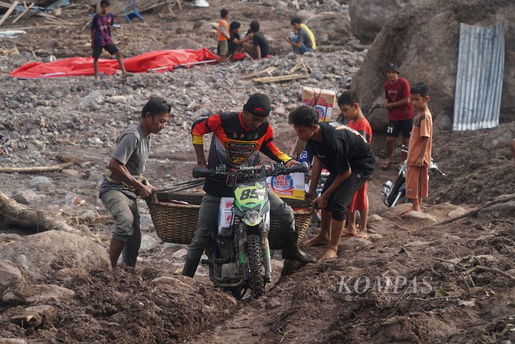 Pengendara motor <i>trail</i> dibantu warga berusaha melewati bekas lokasi banjir bandang terparah untuk mengantarkan bantuan logistik kepada korban bencana di Kampung Langgai, Nagari Ganting Mudik Utara Surantih, Kecamatan Sutera, Kabupaten Pesisir Selatan, Sumatera Barat, Rabu (13/3/2024). 