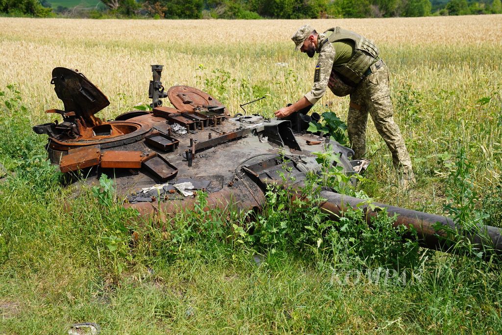  Anggota militer Ukraina sedang memeriksa bagian tank milik Rusia yang hancur di sebuah ladang gandum di desa Mala Rohan, Provinsi Kharkiv, Ukraina, Selasa (5/7/2022). Banyak bahan peledak dan ranjau yang belum dijinakkan tersebar di ladang pertanian warga. 