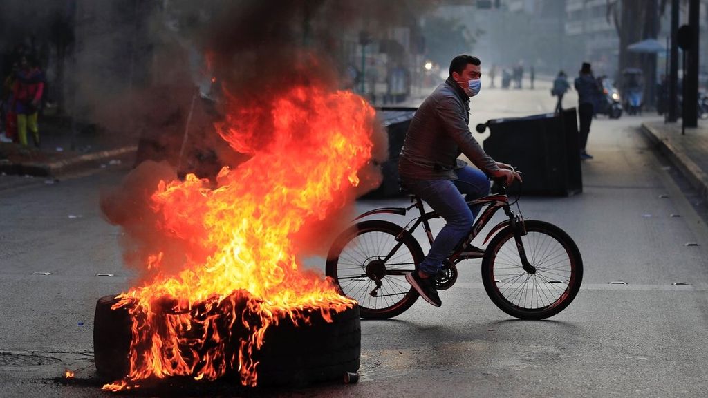 Seorang pria mengendarai sepedanya melewati blokade ban yang dibakar oleh pengunjuk rasa di salah satu jalan utama di Beirut, Lebanon, Senin (29/11/2021). 