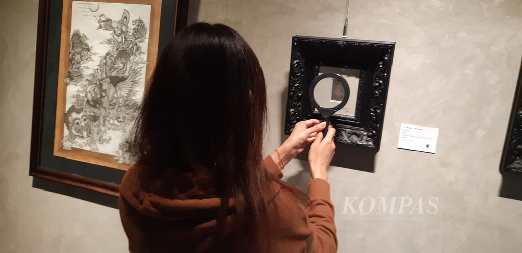 Pengunjung menggunakan kaca pembesar ketika menyaksikan lukisan kecil khas Desa keliki, Gianyar, Bali, yang ditampilkan dalam pameran bersama bertajuk "Roaring into Prosperity" di Galeri Artchange, Pacific Place, Jakarta, Sabtu (16/3/2024).