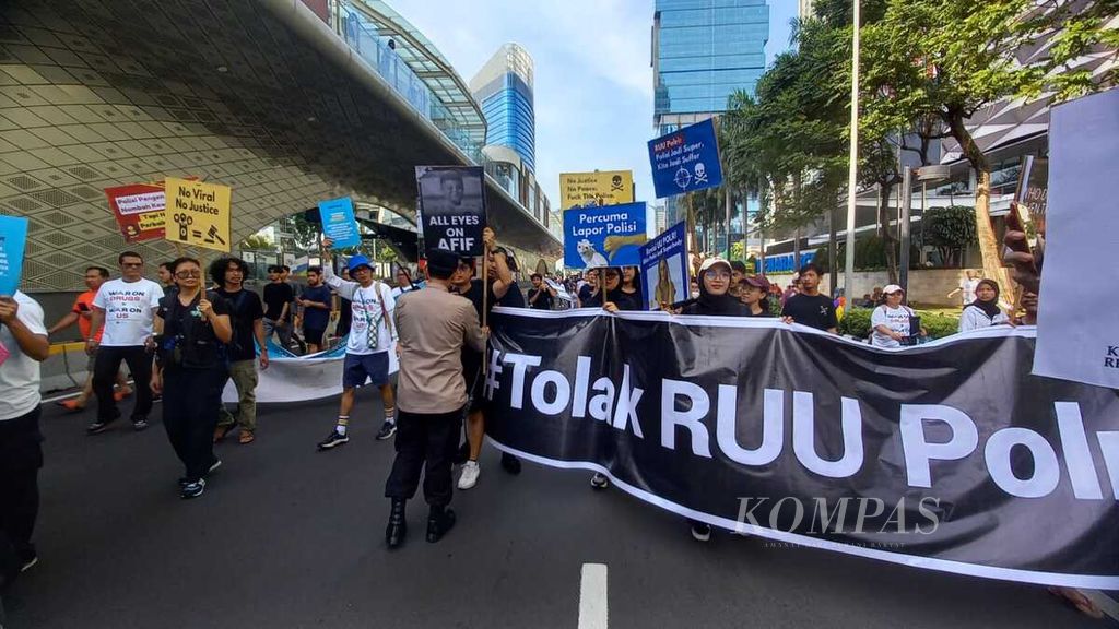 Seorang anggota kepolisian mencoba menghadang Aliansi Masyarakat Sipil untuk Reformasi Kepolisian ketika melakukan aksi penolakan terhadap revisi Undang-Undang Polri saat pelaksanaan hari bebas kendaraan bermotor (<i>car free day</i>), Minggu (30/6/2024) di Jakarta. Masyarakat sipil menolak RUU Polri yang menambah banyak kewenangan kepolisian.