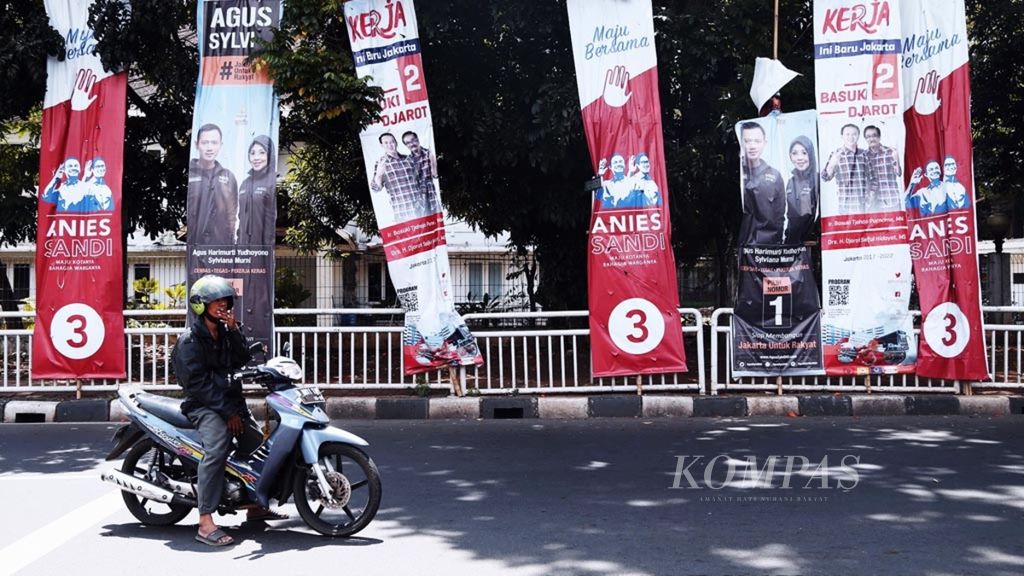 Warga melintas di depan alat peraga kampanye pasangan calon Gubernur dan Wakil Gubernur DKI Jakarta di sekitar kawasan Cikini, Jakarta, Senin (2/1/2017).