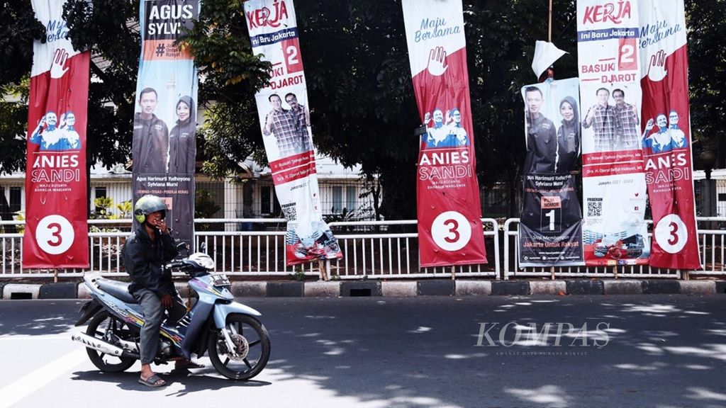 Warga melintas di depan alat peraga kampanye pasangan calon gubernur dan wakil gubernur DKI Jakarta di kawasan Cikini, Jakarta Pusat, Senin (2/1/2017).