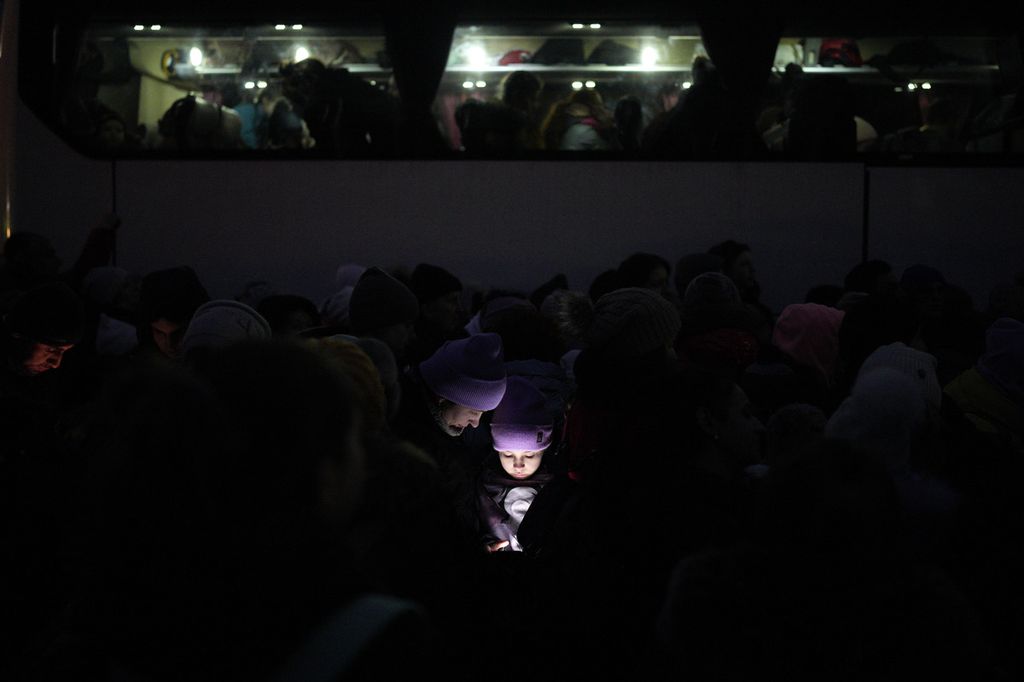 Wajah seorang anak dan orangtuanya disinari cahaya yang berasal dari layar gawai ketika mereka tengah menanti izin masuk ke wilayah perbatasan Polandia di Shehyni, Ukraina, Minggu (6/3/2022). Hingga saat ini, diperkirakan 1,5 juta warga Ukraina telah mengungsi ke sejumlah negara di sekitar. 