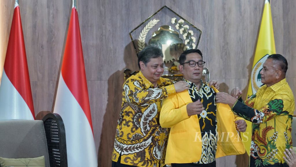 Ketua Umum Partai Golkar Airlangga Hartarto (kiri) dibantu Sekretaris Jenderal Partai Golkar Lodewijk Freidrich Paulus (kanan) memakaikan jas partai kepada Gubernur Jawa Barat Ridwan Kamil (tengah) saat berlangsung pertemuan di Kantor DPP Partai Golkar, Slipi, Jakarta, Rabu (18/1/2023).