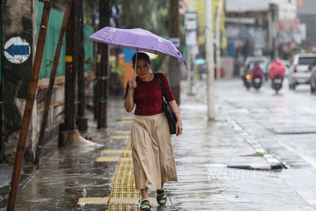 A resident walks with an umbrella during a rainy day on Jatinegara Barat Street in Jakarta on Monday (4/3/2024). The Meteorology, Climatology, and Geophysics Agency predicts that the Jabodetabek area, some parts of southern Sumatra, and Java Island is still in the peak of the rainy season, which could potentially cause extreme weather conditions for the next week.
