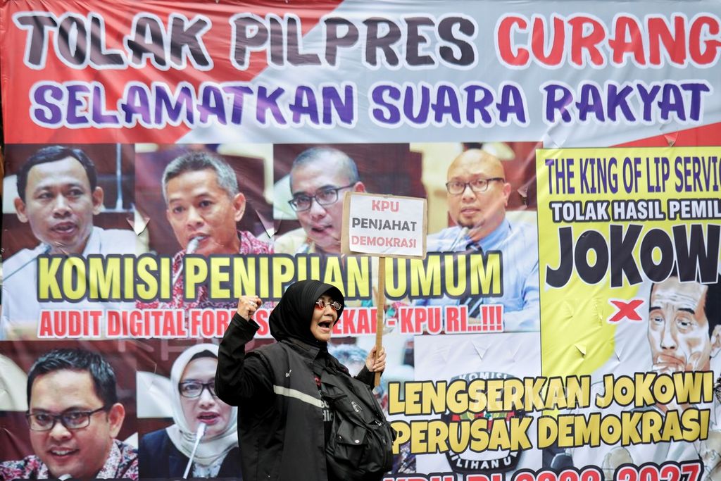 Seorang peserta aksi berdiri di depan spanduk berisi tuntutan demonstran di depan Kantor Komisi Pemilihan Umum (KPU), Jakarta, Rabu (21/2/2024). Peserta aksi yang tergabung ke dalam Poros Buruh menggelar demonstrasi di depan Kantor KPU.