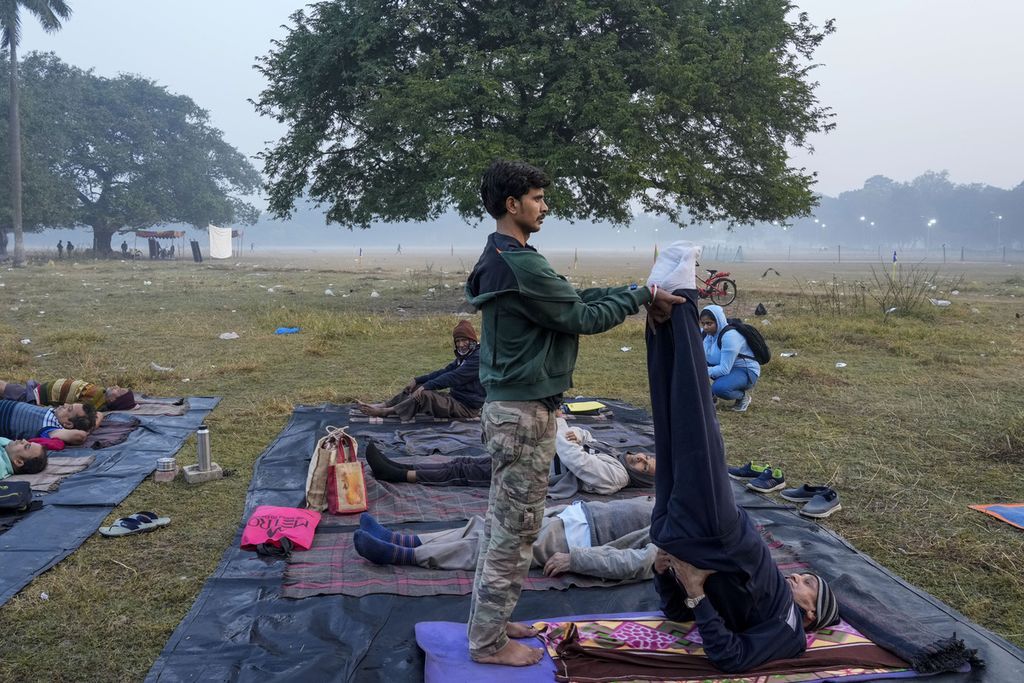 A man assisted others in practicing yoga amidst morning fog in an open space in Kolkata, India on December 30, 2023.