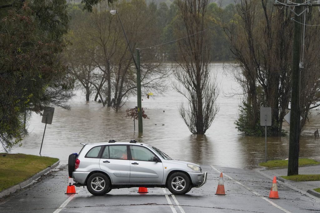 Sebuah mobil diparkir melintang di tengah jalan untuk memblokir jalur yang teredam banjir di kawasan Camden, Sydney, Australia, Senin (4/7/2022). Perubahan iklim yang terjadi sekarang mengubah pola hujan, membuat banjir parah mungkin bakal semakin sering terjadi.