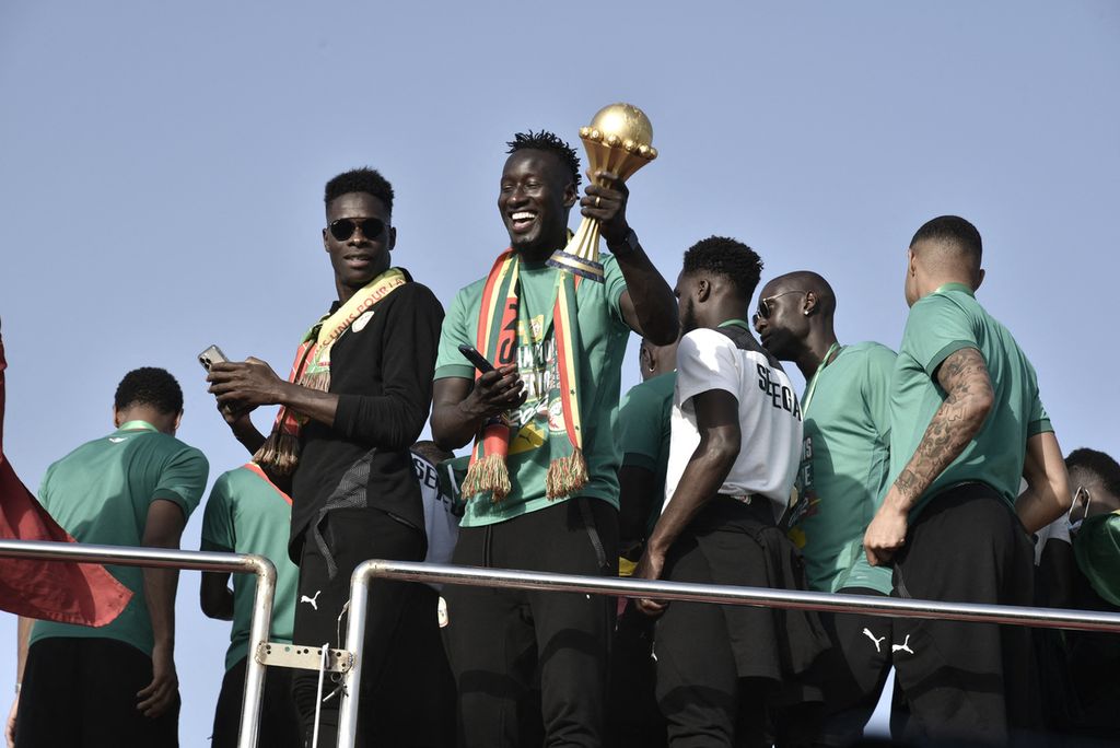 Striker Senegal Famara Diedhiou memegang trofi Piala Afrika bersama para pemain tim lainnya di atas bus di landasan bandara Leopold Sedar Senghor di Dakar Senegal, pada Senin (7/2/2022). 