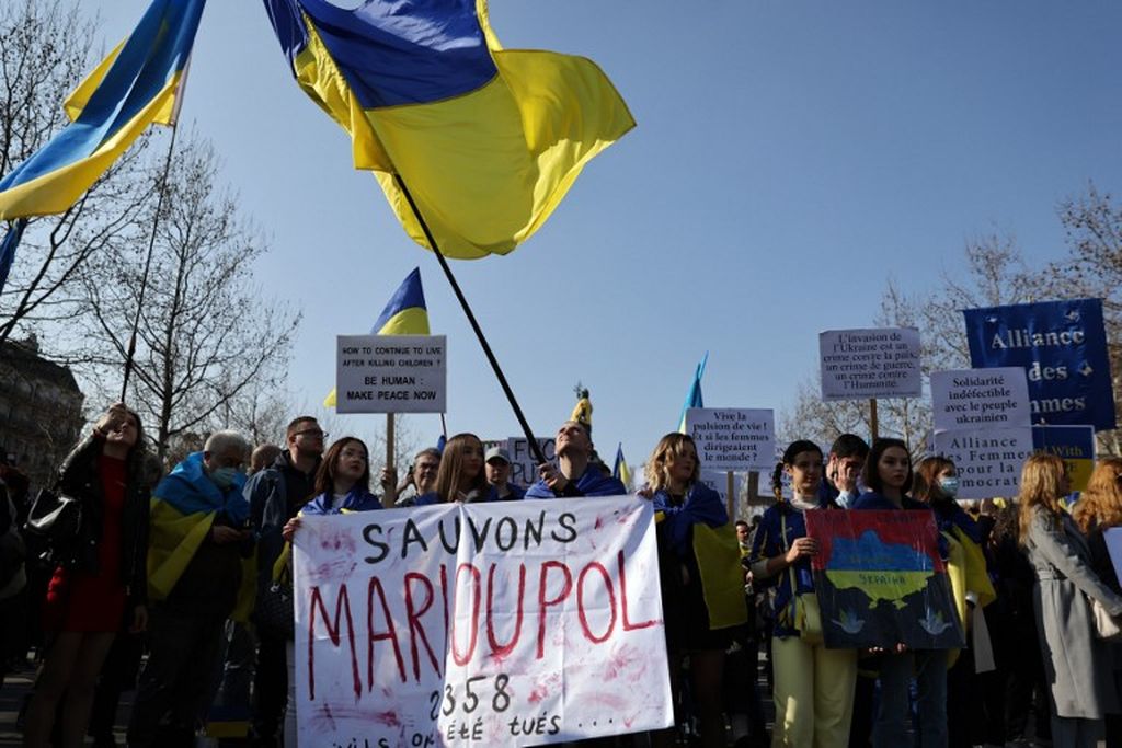 Para pengunjuk rasa mengangkat spanduk bertuliskan "Mari kita selamatkan Mariupol" selama demonstrasi mendukung Ukraina, pada hari ke-24 invasi Rusia ke Ukraina, 19 Maret 2022.  Kini Mariupol, kota pelabuhan di Ukraina selatan, telah jatuh ke tangan Rusia.