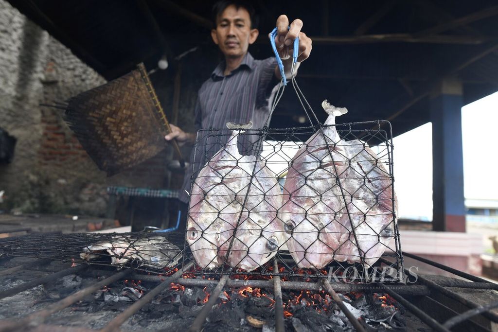 A seller grills fish at a restaurant on the coast of the Indramayu north coast road (pantura) in Eretan, Kandanghaur District, Indramayu Regency, West Java, Friday (22/4/2022).