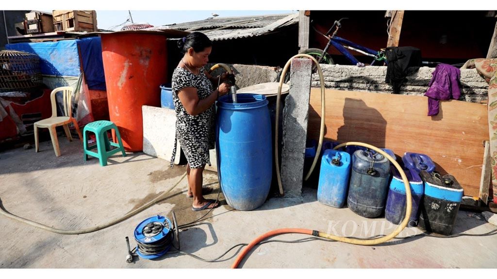 Kasni (43), pedagang air bersih di kawasan Muara Baru, Penjaringan, Jakarta Utara, menyalurkan air dari tandon besar ke rumah pelanggan melalui selang, Kamis (11/7/2019). Warga di sekitar kampung ini masih belum terjangkau pemipaan air.