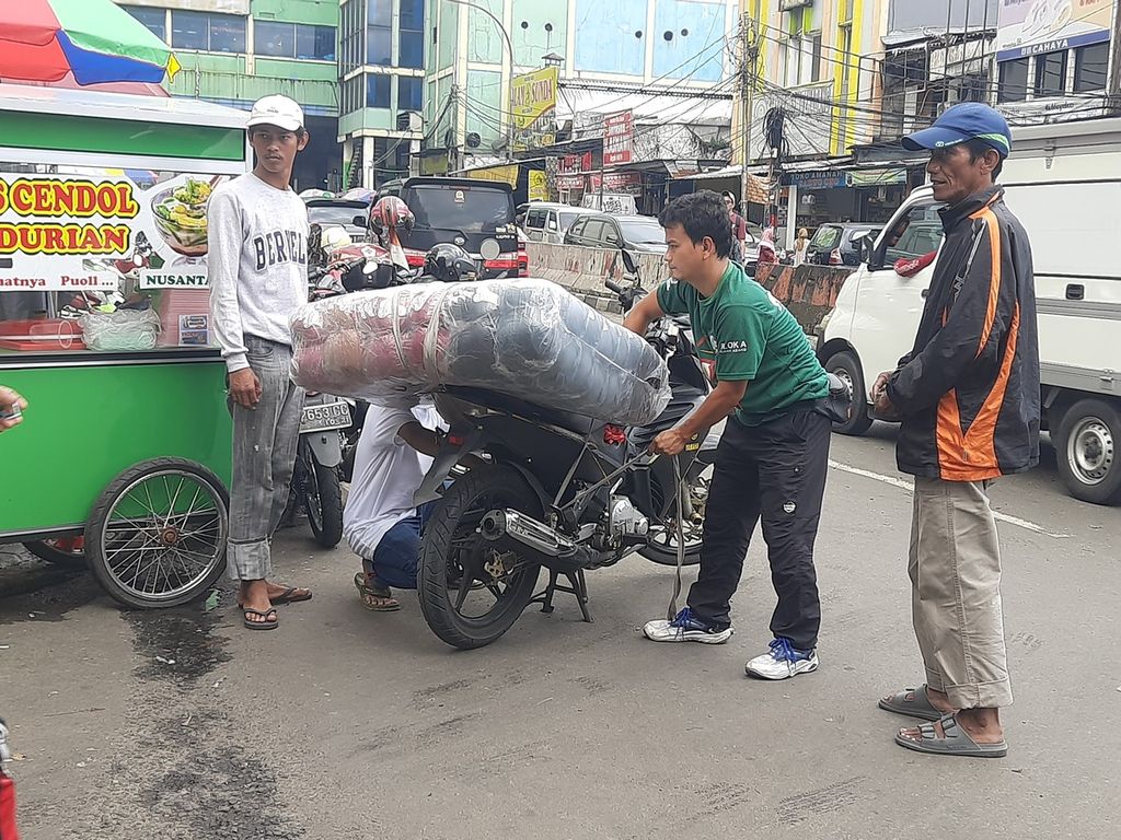 Seorang kuli angkut membantu menyusun barang di atas sepeda motor milik salah satu pelanggannya di Pasar Tanah Abang, Jakarta, Kamis (9/3/2023).