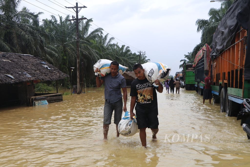 Penumpang bus jurusan Medan-Banda Aceh berjalan kaki membawa barang untuk menembus kemacetan lalu lintas akibat banjir yang merendam sejumlah ruas jalan di Kabupaten Aceh Tamiang, Aceh, selama empat hari, hingga Sabtu (5/11/2022). 