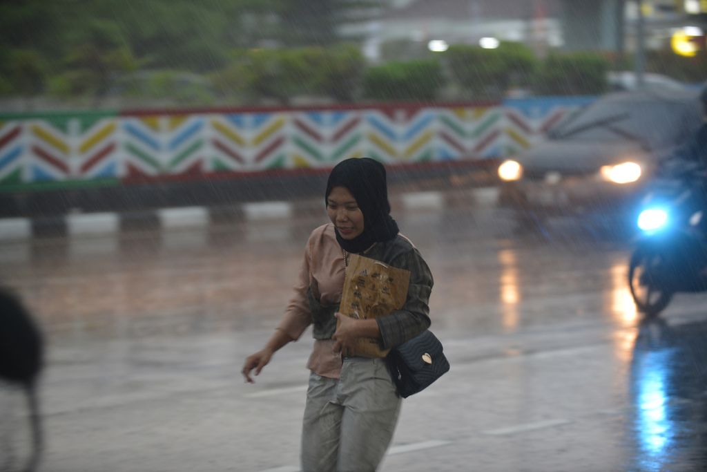 Warga berlari di tengah guyuran hujan di Jalan Kramat Bunder, Jakarta Pusat, Selasa (4/10/2022). 