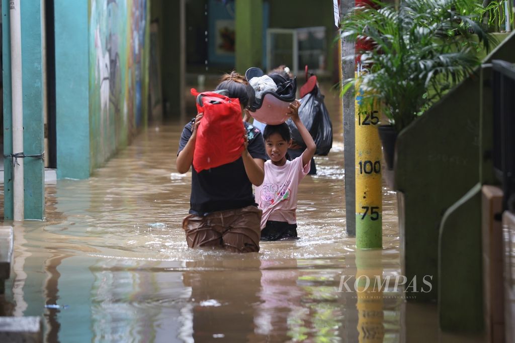 Warga membawa barang bawaan saat melintasi banjir di Kelurahan Kampung Melayu, Kecamatan Jatinegara, Jakarta Timur, Jumat (15/3/2024).