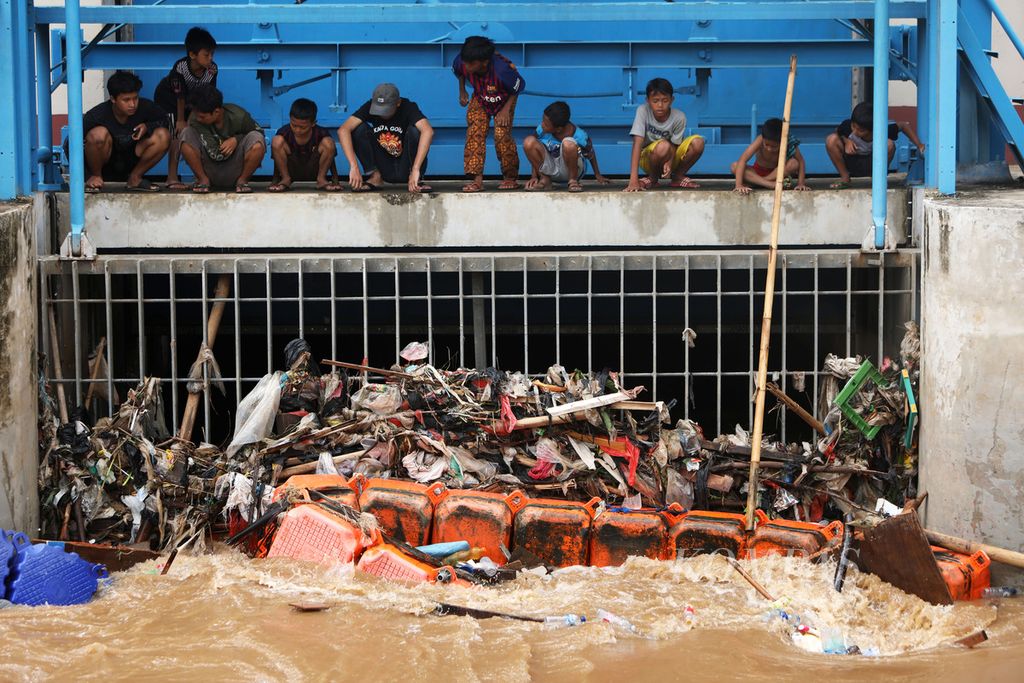 Warga melihat sampah yang tersangkut di Pintu Air Manggarai, Jakarta, Kamis (2/1/2020). Berbagai jenis sampah, seperti plastik, ranting pohon, dan sampah rumah tangga, banyak terbawa arus Sungai Ciliwung.