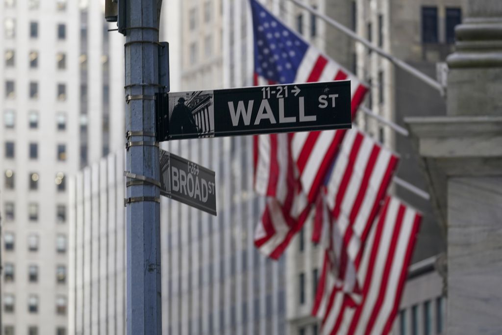 Dalam foto yang diambil pada Jumat (14/1/2022) ini tampak tanda petunjuk jalan Wall Street di New York City dengan latar belakang bendera Amerika Serikat.