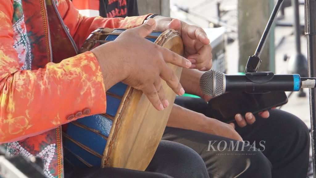 Seniman madihin, Ahmad Syarani, memainkan <i>tarbang</i> (gendang khas suku Banjar) yang mengiringi madihinnya di depan anak-anak di Dermaga Pasar Terapung Muara Kuin, Banjarmasin,  Sabtu (9/9/2023). 