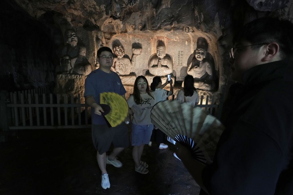 Wisatawan berfoto di depan patung Buddha yang dipahat pada dinding gua tak jauh dari Kuil Lingyin, Hangzhou, China. Foto diambil pada Senin (3/7/2023).