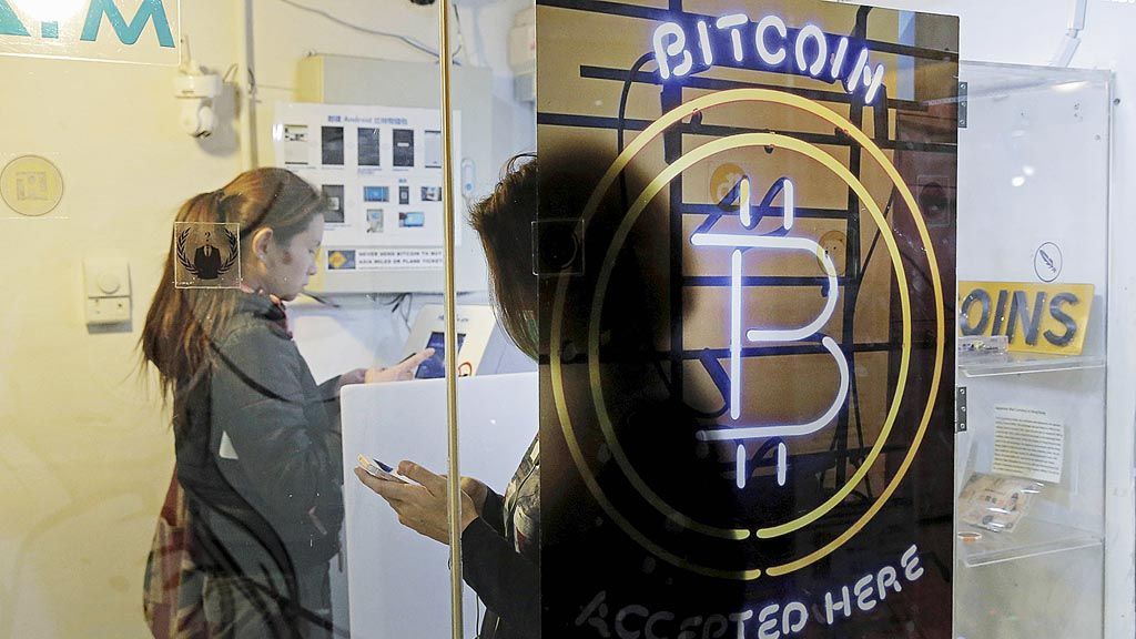 Warga   sedang menggunakan ATM bitcoin di Hong Kong, 8 Desember 2017. Meluasnya pemanfaatan  bitcoin  sebagai sarana investasi membuat otoritas moneter di beberapa negara memberi perhatian terhadap mata uang virtual itu (foto atas). Koleksi koin bitcoin ditampilkan dalam gambar ilustrasi yang fotonya diambil pada 8 Desember 2017 