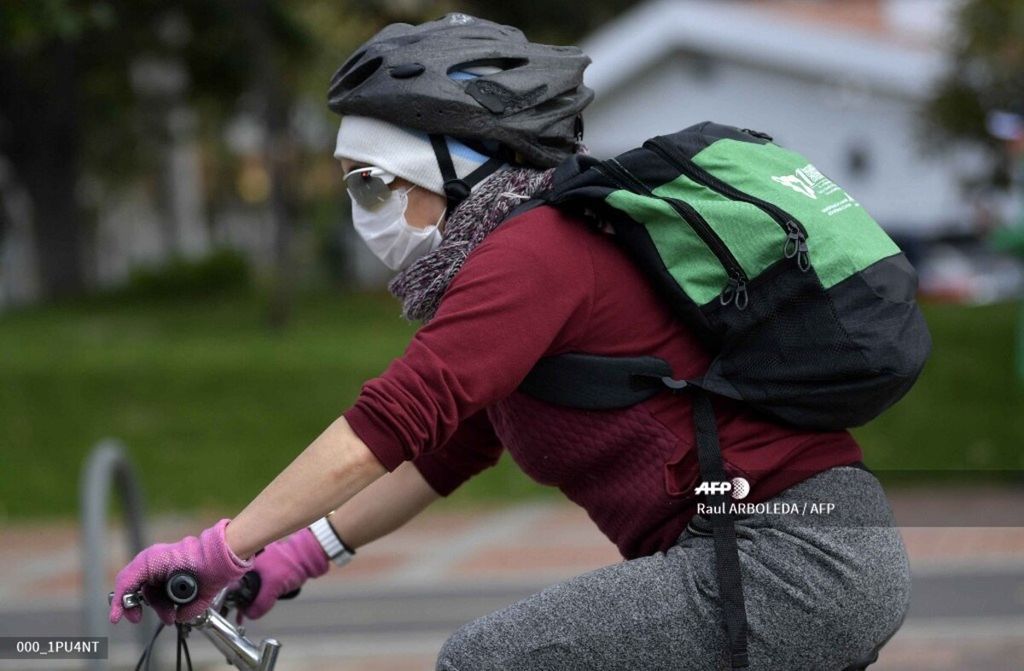 A woman uses a face mask as a precautionary measure in the face of the global COVID-19 coronavirus pandemic, as she rides a bike in Bogota on March 12, 2020. – Colombia declared on March 12, 2020 a “Health Emergency” due to the new coronavirus pandemic, a figure that allows it to take exceptional measures such as prohibiting the disembarkation of cruise ships and the holding of public events with more than 500 attendees. 