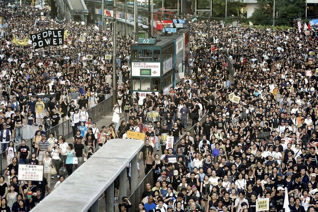 Dalam foto bertanggal 1 Juli 2003 ini terlihat trem yang terjebak di antara ribuan orang yang berunjuk rasa memprotes undang-undang kontroversi, yang disebut Pasal 23, di Hong Kong. Pada 23 Maret 2024, Hong Kong mulai memberlakukan Pasal  23 itu. 