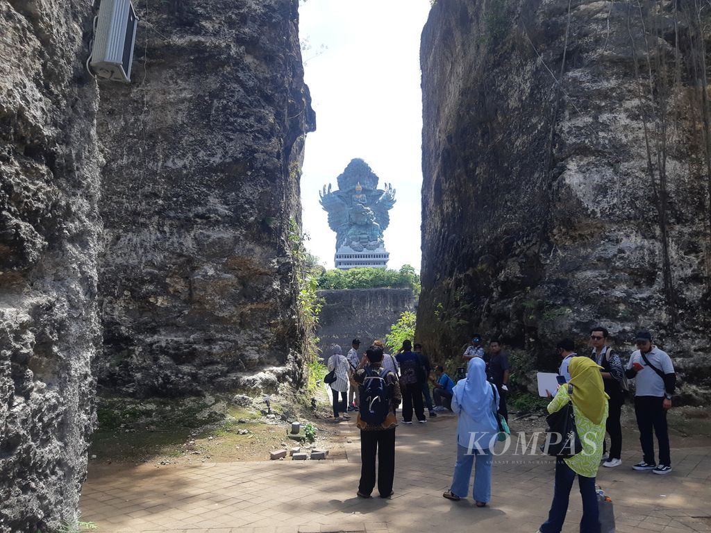 Dari balik tebing, wisatawan menyaksikan patung raksasa Garuda Wisnu Kencana di Taman Budaya Garuda Wisnu Kencana, Kabupaten Badung, Bali, Kamis (8/12/2022). Patung karya seniman Nyoman Nuarta itu merupakan salah satu patung tertinggi di dunia.