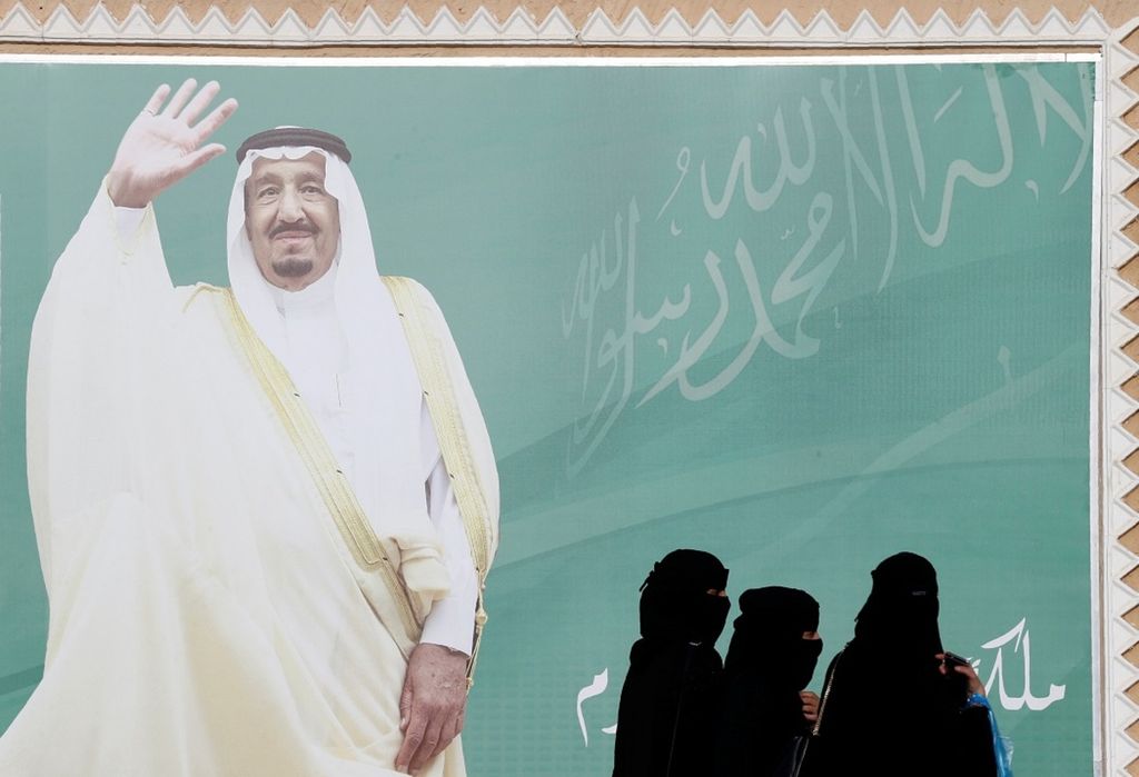 Para perempuan Arab Saudi berjalan melewati poster bergambar Raja Salman bin Abdulaziz al-Saud saat berlangsung Festival Kebudayaan Janadriyah di pinggiran Riyadh, Arab Saudi, 12 Februari 2018.