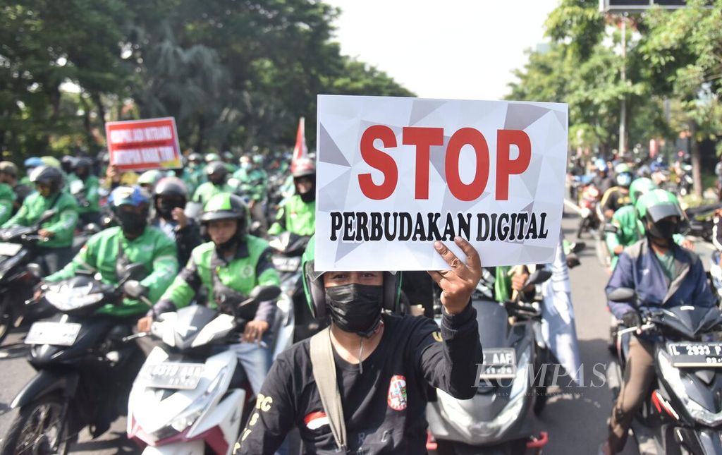 Seorang pengunjuk rasa membawa poster tuntutan saat pengendara ojek daring melakukan unjuk rasa di depan Kantor Dinas Perhubungan Jawa Timur, Surabaya, Jawa Timur, Kamis (24/3/2022). 
