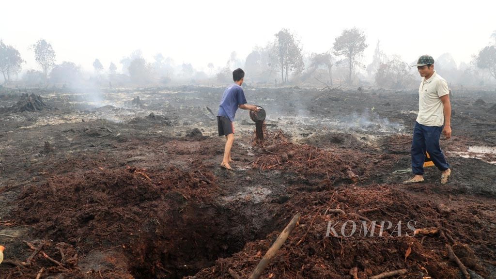 Warga secara manual membasahi lahan gambut yang masih mengeluarkan asap di Desa Merbau, Kecamatan Bunut, Kabupaten Pelalawan, Riau, Selasa (17/9/2019). 