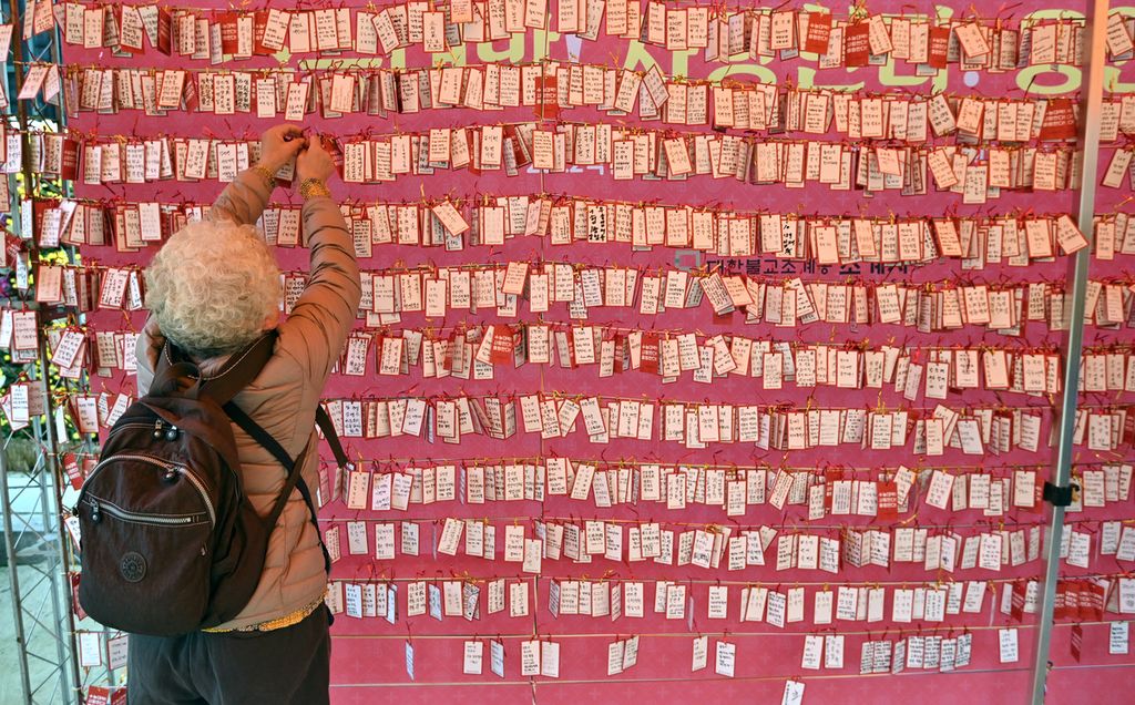 Seorang wanita menempelkan kartu nama dengan harapan kesuksesan siswa mengikuti ujian <i>suneung</i> di Kuil Jogyesa, Seoul, Korea Selatan, Kamis (18/11/2021). 