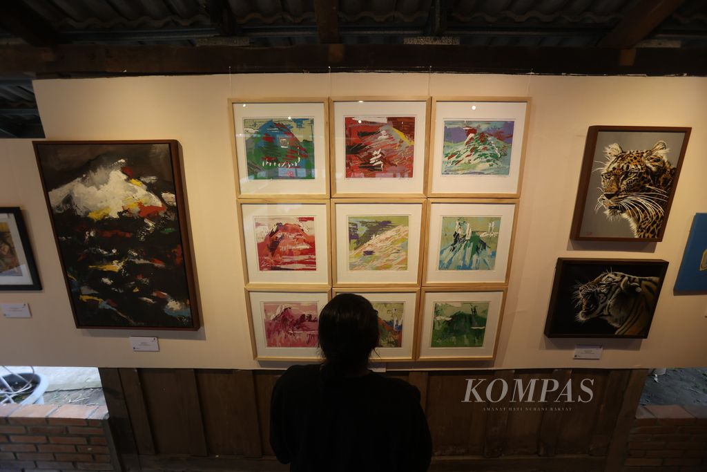 Pengunjung melihat lukisan yang ditampilkan dalam pameran seni rupa bertajuk Adem Ayem di pendopo Sekolahane Pak Petroek, kompleks Omah Petroek, Desa Hargobinangun, Pakem, Sleman, DI Yogyakarta, Kamis (25/7/2024).