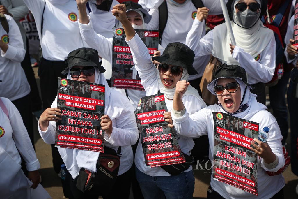 Tenaga kesehatan berteriak sembari menunjukkan poster kritik dalam aksi menolak pengesahan Rancangan Undang-Undang (RUU) Kesehatan di depan Kompleks Parlemen, Jakarta, Selasa (11/7/2023).