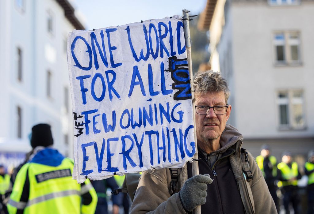 Seorang pengunjuk rasa memegang poster saat demonstrasi di Davos, Swiss, Minggu (14/1/2024), menjelang Pertemuan Tahunan Ke-54 Forum Ekonomi Dunia. 