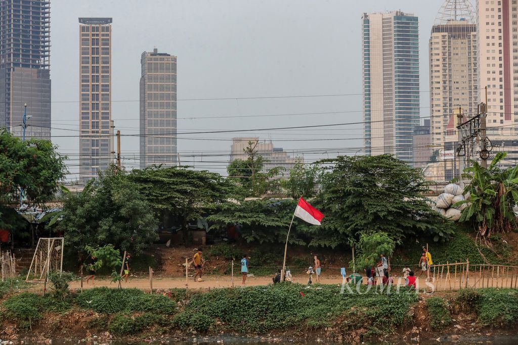 Anak-anak dan remaja bermain bola di bantaran Kanal Banjir Barat, Tanah Abang, Jakarta, Rabu (5/7/2023). Kurangnya lahan bermain membuat anak-anak di kawasan Petamburan memanfaatkan lahan kosong di bantaran kali.