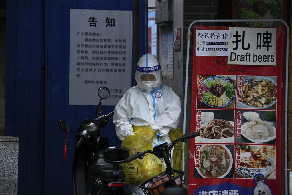 Seorang petugas kesehatan mengenakan pakaian pelindung diri keluar dari pemukiman di Beijing yang tengah menjalani karantina. Petugas tersebut usai mengambil sampel dari warga pemukiman tersebut. Foto diambil pada Minggu (26/6/2022). 