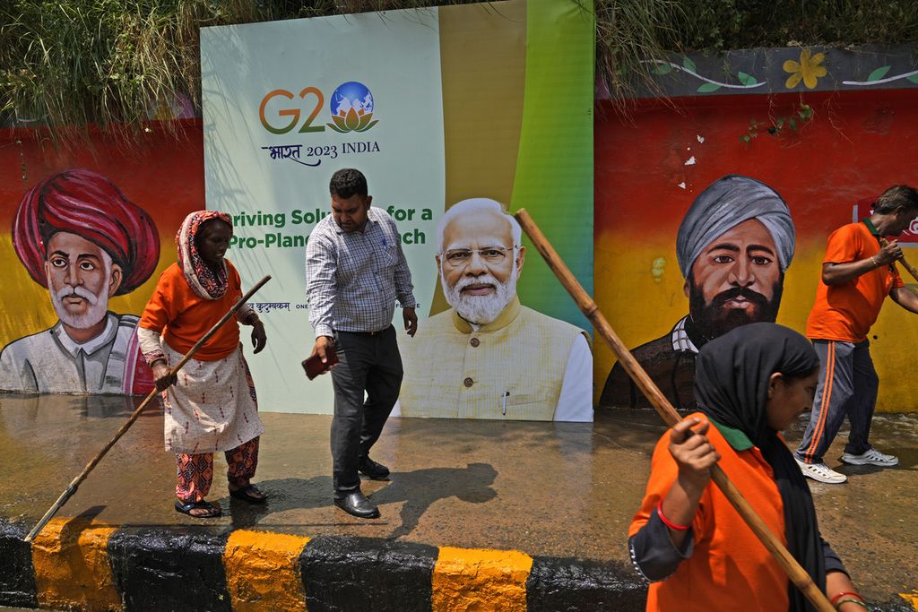 Pekerja kota mencuci jalan dekat papan reklame yang menampilkan Perdana Menteri India Narendra Modi dan lukisan dinding pejuang kemerdekaan India menjelang KTT G20 di New Delhi, India, 7 September 2023.